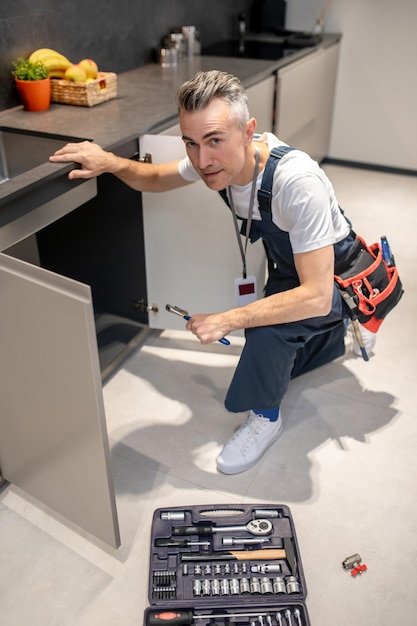 Free photo housework top view of man in overalls with badge crouching near sink a