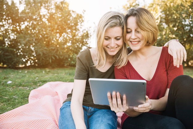 Hugging women browsing tablet in park