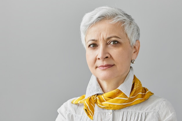 Free photo human facial expressions, feelings, emotions and reaction. close up beautiful middle aged female pensioner with short gray hair frowning eyebrows, having concentrated serious look