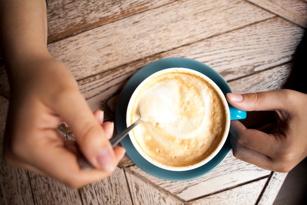 Human hand holding coffee spoon and stirring hot coffee on wooden table