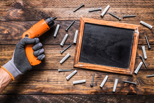 Human hand holding cordless drill near screws surrounding blank slate