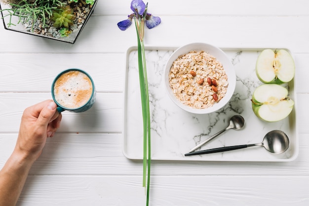 Human hand holding a cup of coffee with delicious breakfast on wooden plank