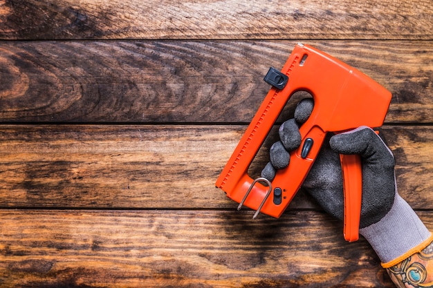 Human hand holding staple gun on wooden background