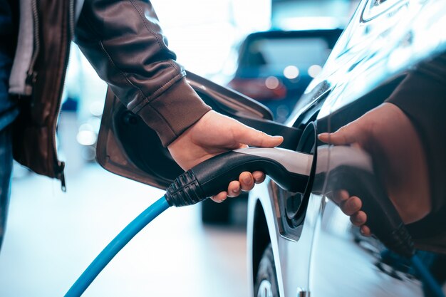 Human hand is holding electric car charging connect to electric car