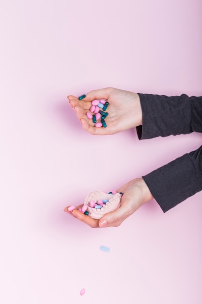 Human hand pouring pills in dental model plaster cast over pink backdrop