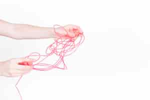 Free photo human hand trying to untangle red wire on white background