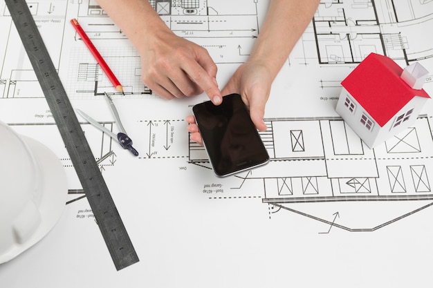 Free Photo human hand using cellphone over blueprint at workplace