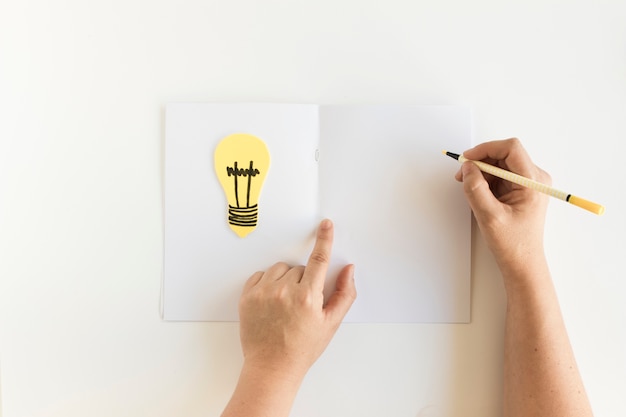 Free Photo human hand writing on card with light bulb