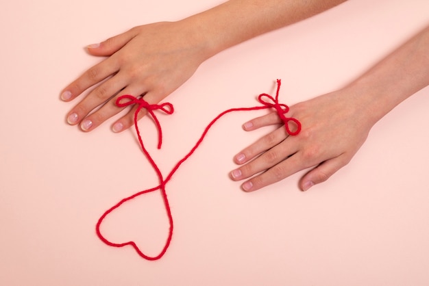 Human hands connected with red thread in heart shape