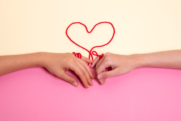 Human hands connected with red thread in heart shape