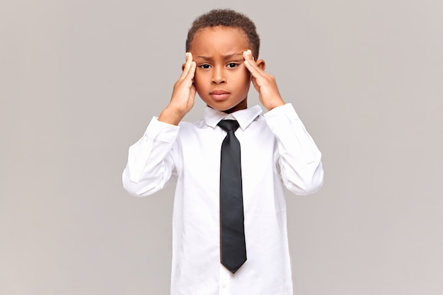 Human reaction, feelings and attitude.  frustrated unhappy African pupil in school uniform massaging temples, suffering from headache, being stressed with lot of home assignment