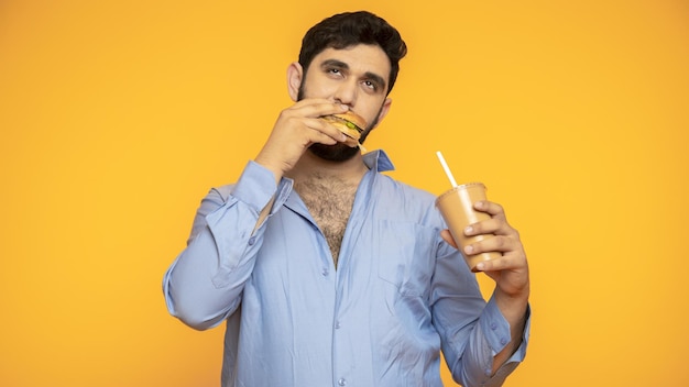 Hungry handsome man holds a hamburger in his hand on yellow background