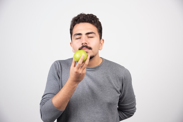 Hungry man smells green apple on gray.