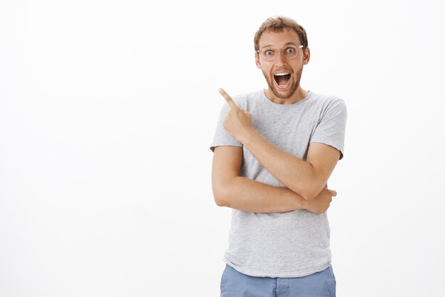 Husband being surprised and happy like child receiving awesome gift from wife pointing at upper left corner joyfully smiling broadly staring impressed and enthusiastic