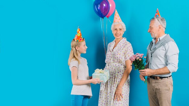 Husband and granddaughter giving gift to senior woman on blue backdrop