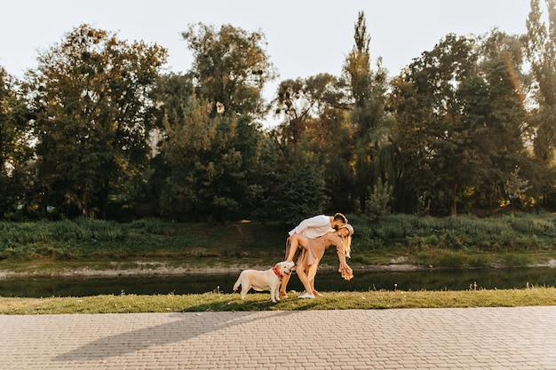 Free Photo husband and wife fooling around and dancing tango in park near pond while walking with labrador.