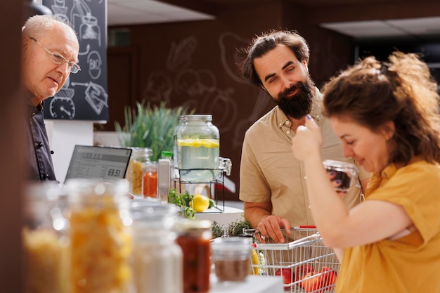 Free Photo husband and wife at zero waste supermarket checkout counter with shopping basket full of organic food. customers waiting for their pantry staples to be weighted with electronic scale in local shop