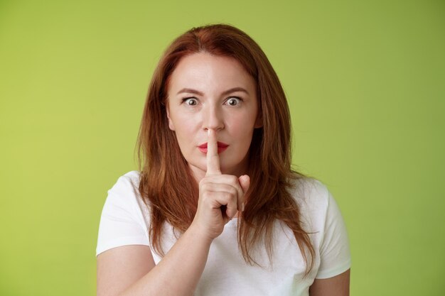 Hush not say that worried shocked redhead middleaged wife demand keep mouth shut shushing ask silence stop spread false rumours stare camera hold index finger pressed lips taboo gesture