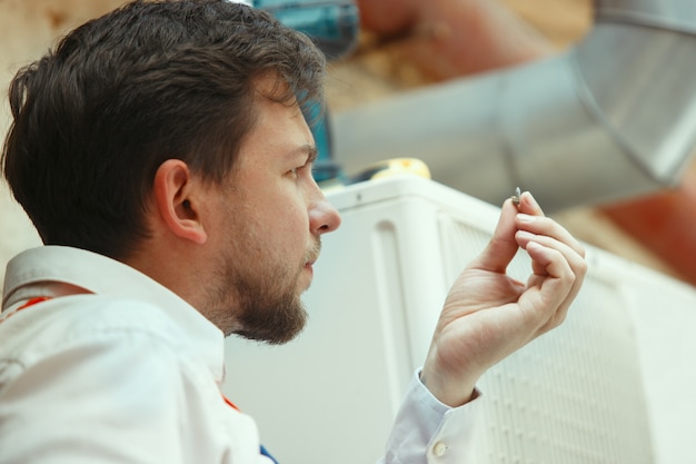 HVAC technician working on a capacitor part for condensing unit. Male worker or repairman in uniform repairing and adjusting conditioning system, diagnosing and looking for technical issues.