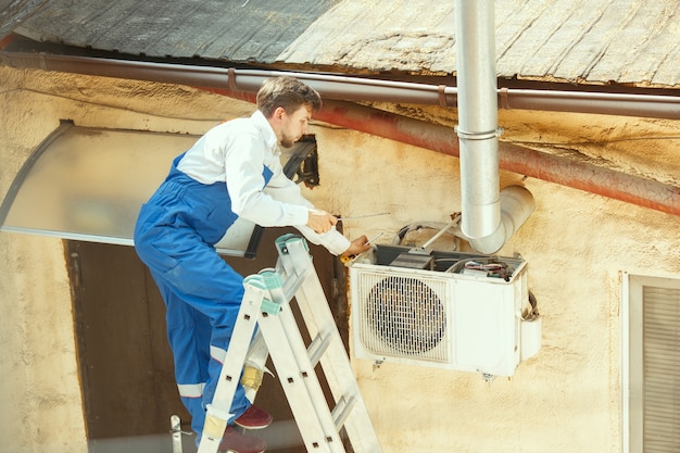 Free photo hvac technician working on a capacitor part for condensing unit. male worker or repairman in uniform repairing and adjusting conditioning system, diagnosing and looking for technical issues.