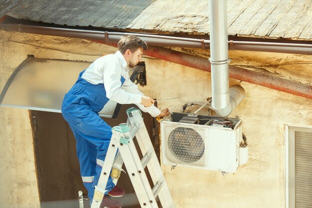 HVAC technician working on a capacitor part for condensing unit. Male worker or repairman in uniform repairing and adjusting conditioning system, diagnosing and looking for technical issues.