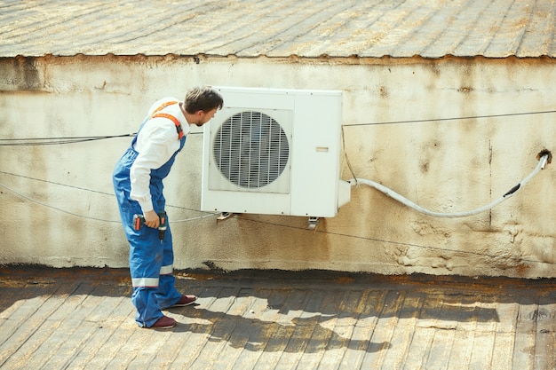 Free Photo hvac technician working on a capacitor part for condensing unit. male worker or repairman in uniform repairing and adjusting conditioning system, diagnosing and looking for technical issues.