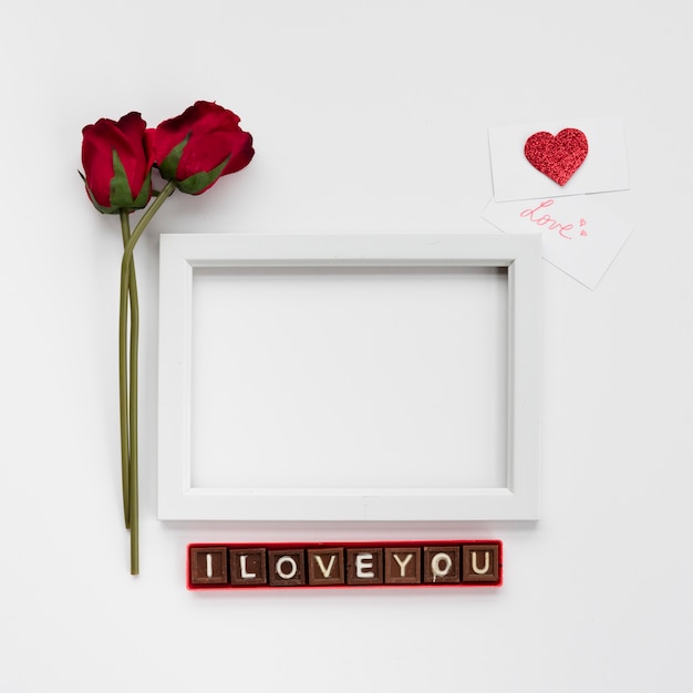 I love you inscription on chocolate pieces near photo frame, flowers and cards