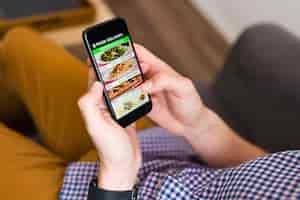 Free photo i'm hungry. hands of a man looking at a food delivery app on his smartphone and ordering dinner online