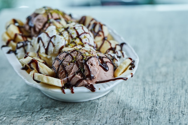 Free photo ice-cream with bananas, chocolate and sprinkles on the white plate