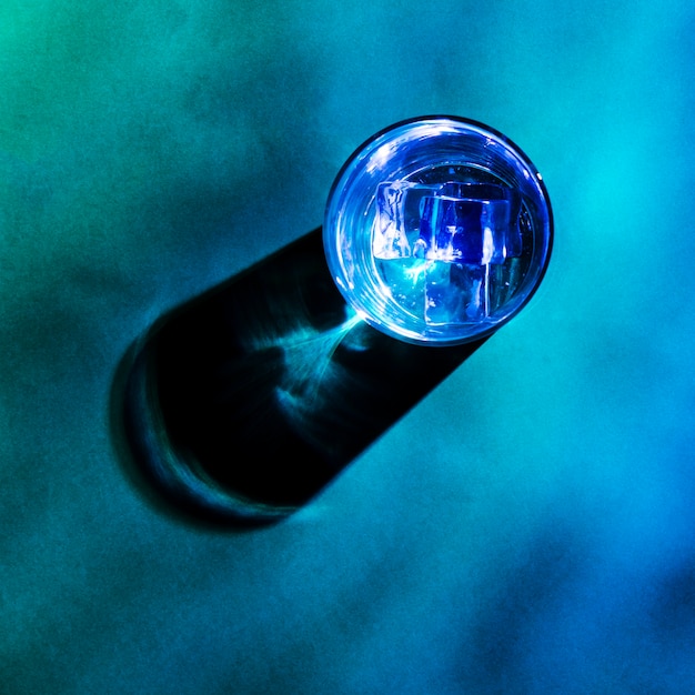 Ice cubes in blue glass with shadow on colored background