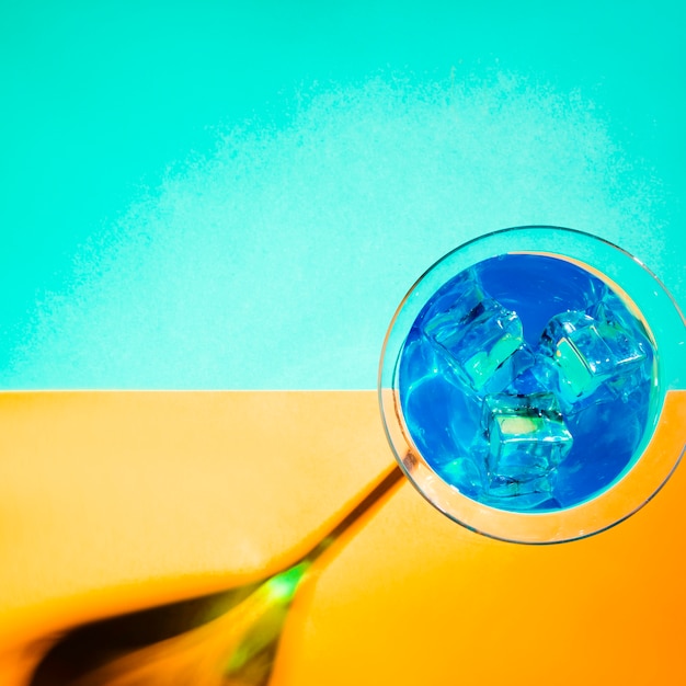 Ice cubes in the blue martini glass on turquoise and yellow background