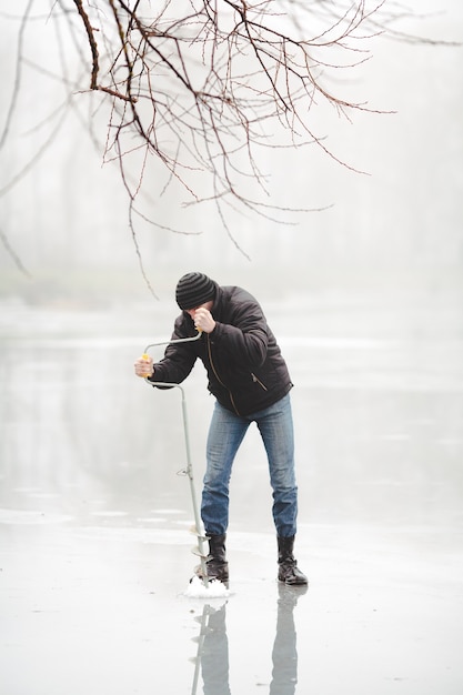 Free photo ice fisherman drilling a hole with a power auger on frozen lake