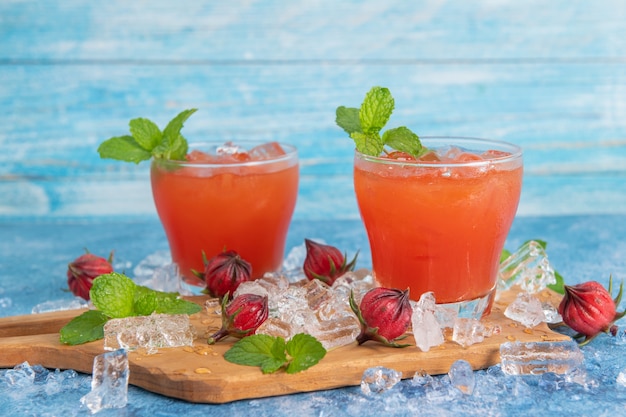 Iced roselle tea glass with fresh roselle fruit on wooden table for healthy herbal drink concept. herbal organic tea for good healthy.