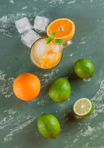 Free photo icy detox water in a cup with oranges, mint, limes flat lay on a plaster surface