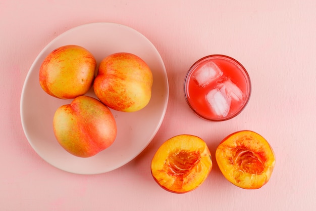 Free photo icy juice in a glass with nectarines flat lay on a pink surface