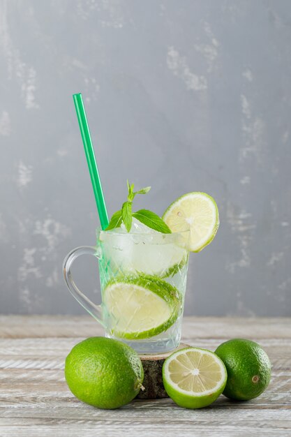 Icy mojito cocktail in a cup with limes, mint, straw side view on wooden and plaster wall