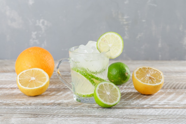 Free photo icy mojito cocktail in a cup with limes, orange, lemon side view on wooden and plaster wall