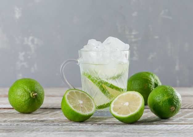 Free photo icy mojito cocktail in a cup with limes side view on wooden and plaster background