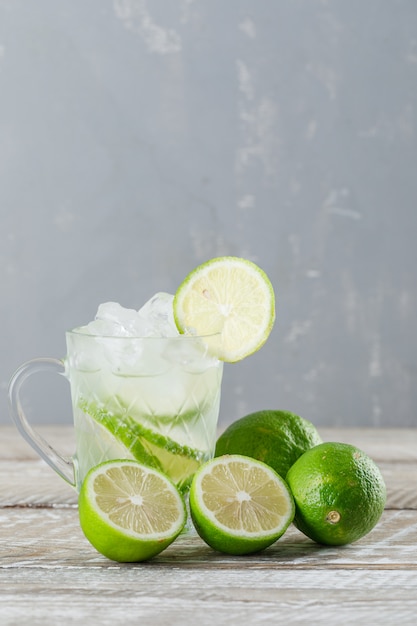 Free Photo icy mojito cocktail with limes in a glass cup on wooden and plaster background, side view.