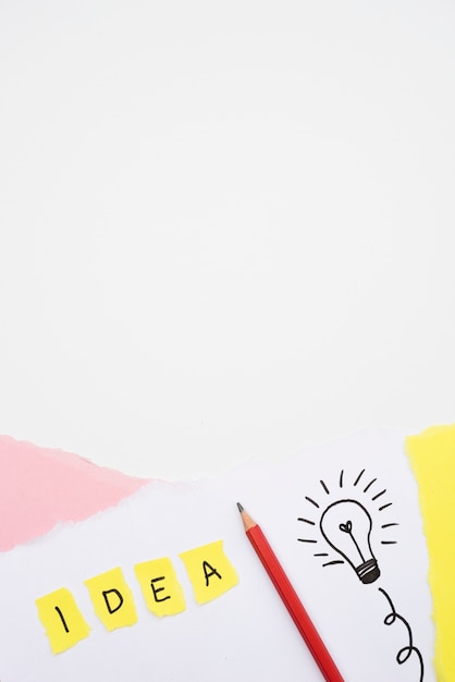 Free photo idea text and hand drawn light bulb with pencil on paper over white backdrop