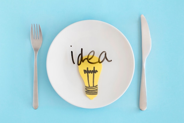 Free photo idea text with yellow light bulb over the white plate with fork and butter knife against blue background