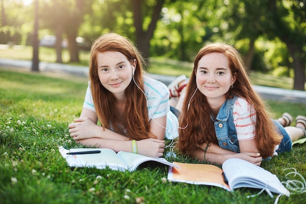 Identical ginger twin sisters studying in a city park. Having a great time in university or school, ready to protect each other from bullying. Frienship and support concept.