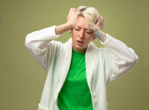 Free photo ill woman with short hair feeling unwell touching her head suffering from strong headache standing over light background