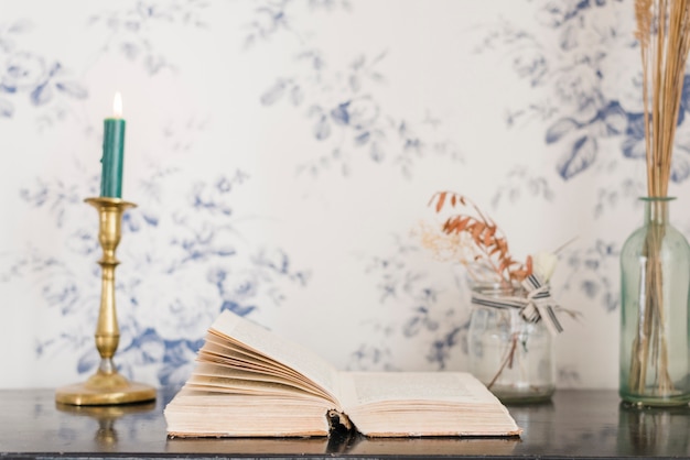 Free photo an illuminated candle and book on desk against wallpaper