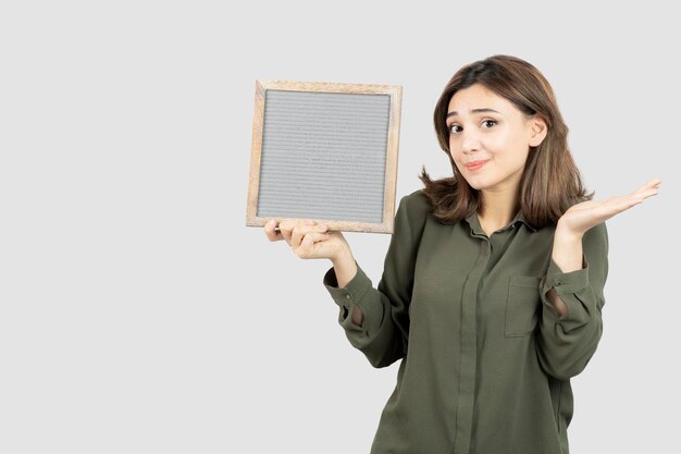 Image of adorable young woman holding empty frame over white. High quality photo