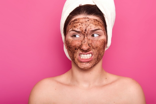 Free photo image of annoyed attractive young model with white towel on her head opening mouth, setting teeth, looking aside, having irratated facial expression. skincare, beauty and treatment concept.