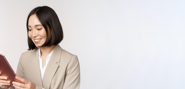 Image of asian businesswoman using digital tablet looking at gadget and smiling working standing against white background