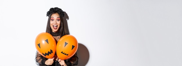 Free photo image of asian girl in evil witch costume holding two orange balloons with scary faces celebrating h