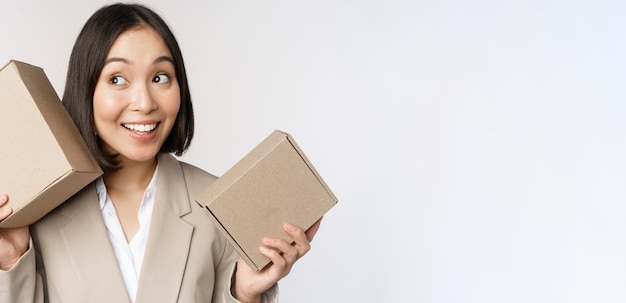 Image of asian saleswoman shaking boxes and guessing whats inside smiling thoughtful standing over white background