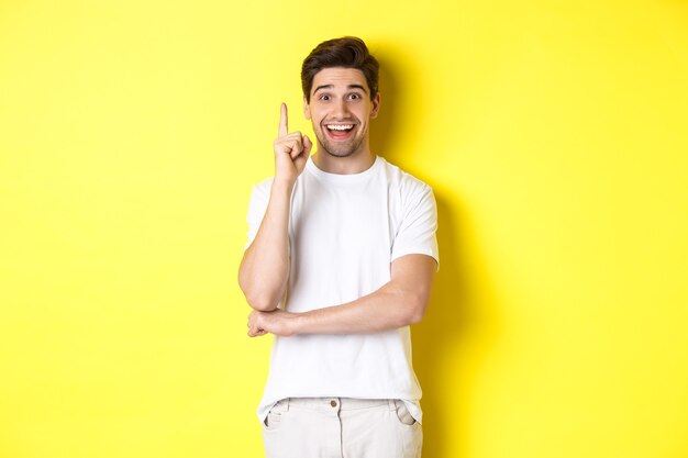 Image of attractive guy having an idea raising finger up and suggesting plan smiling excited standin...